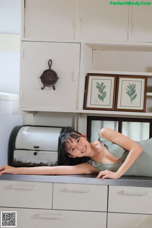 A woman laying on top of a kitchen counter next to a toaster.