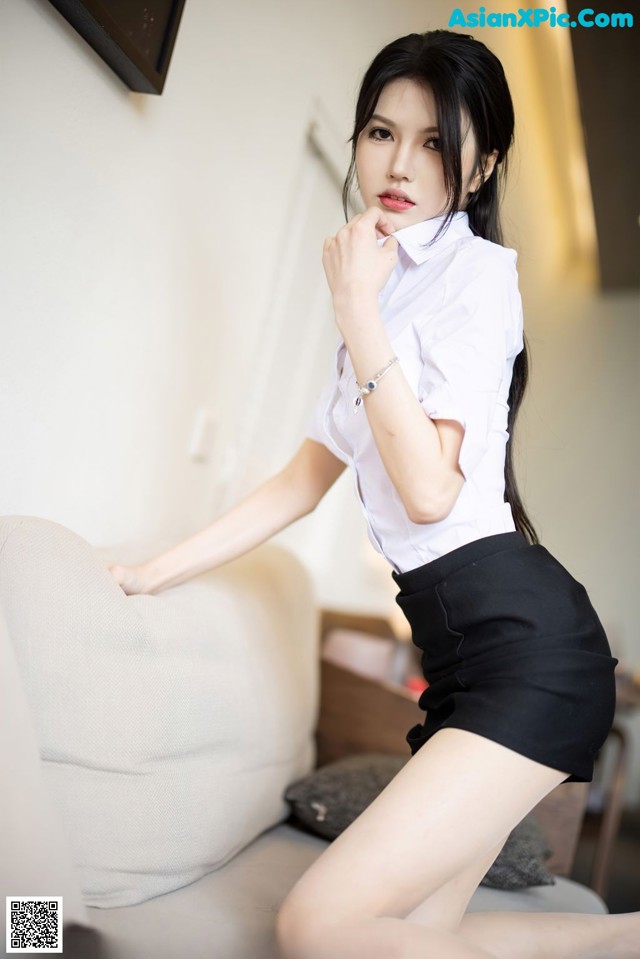 A woman in a white shirt and black skirt posing on a couch.