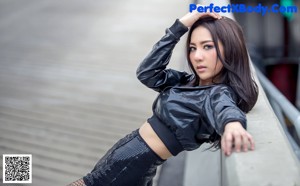 A woman in a black leather jacket leaning against a railing.