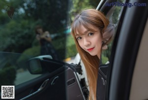 A woman in a black dress standing next to a blue car.