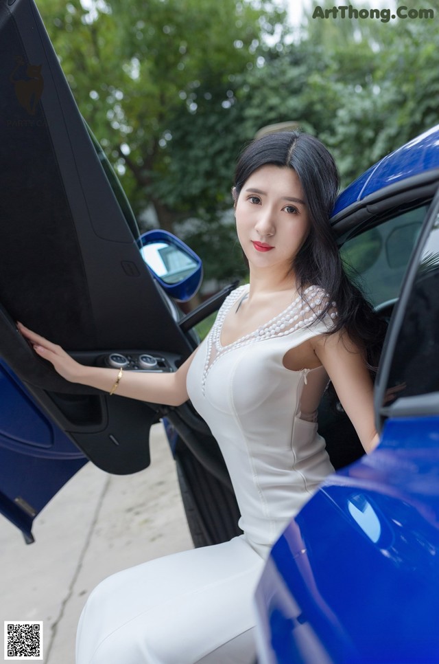 A woman in a white dress sitting in a blue car.