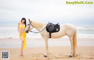 A woman in a white dress riding a white horse on the beach.