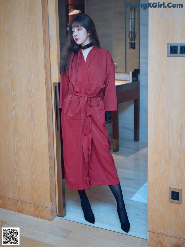 A woman standing in front of a wooden door wearing a red coat.