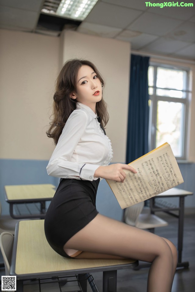 A woman sitting on a desk holding a sheet of music.