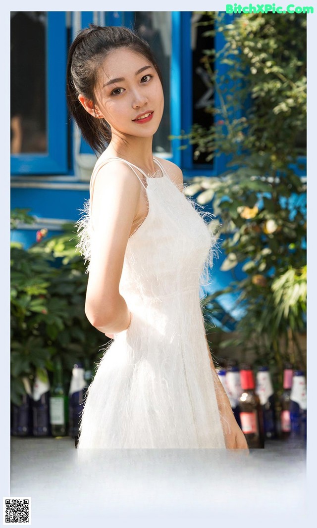 A woman in a white dress standing in front of a blue door.