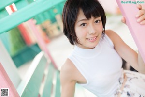 A woman leaning against a pink wall in a white top and skirt.