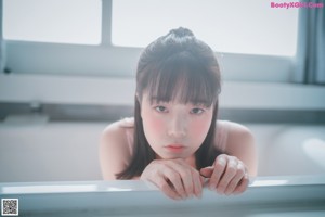 A woman sitting on a bed wearing a pink bodysuit.