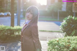 A woman in a brown jacket and blue skirt standing on a sidewalk.