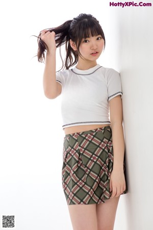 A woman in a white shirt and plaid skirt is posing for a picture.