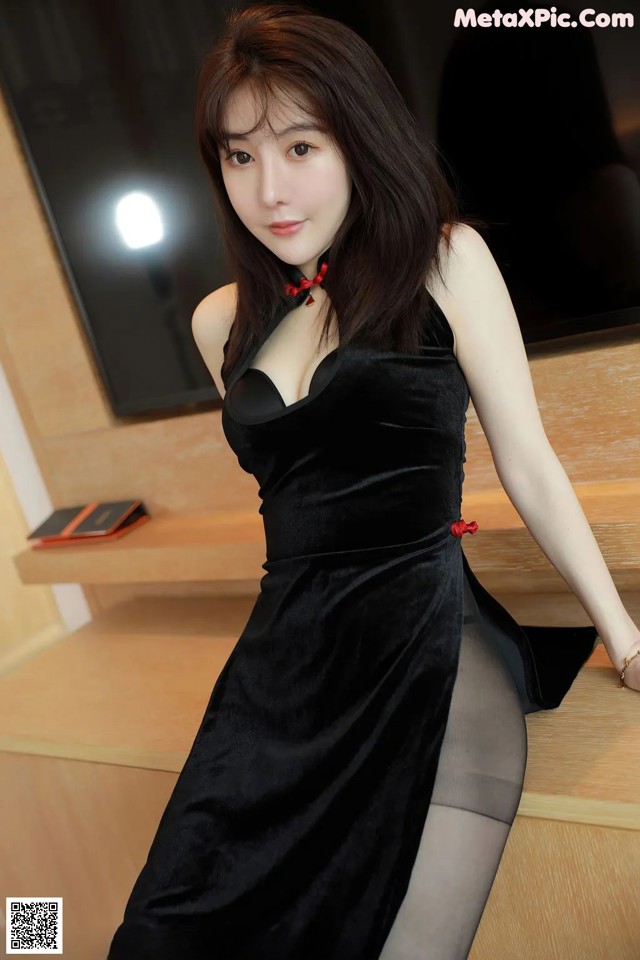 A woman in a black dress sitting on a wooden table.
