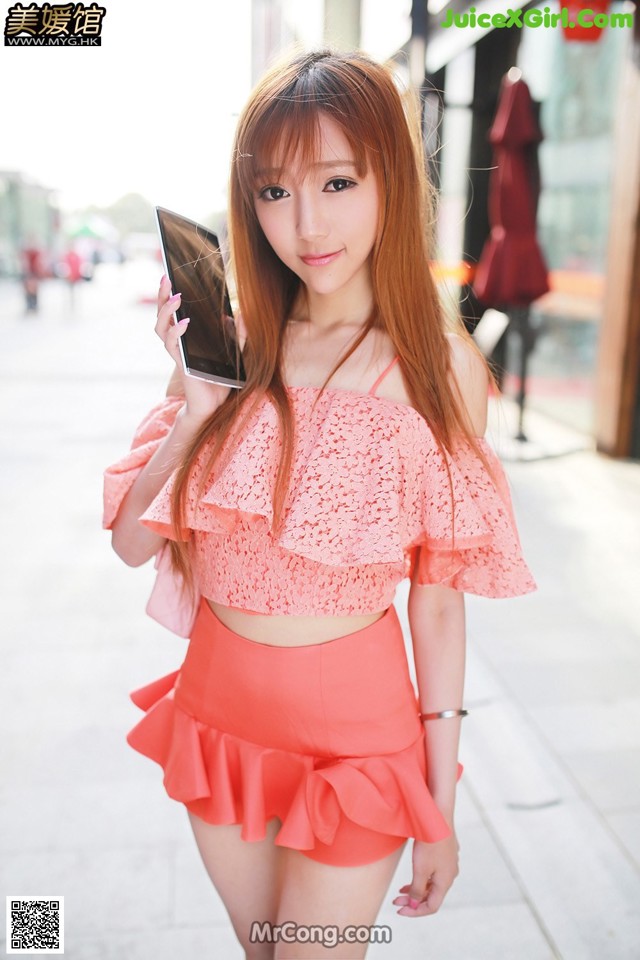 A woman in a pink top and orange skirt holding a cell phone.