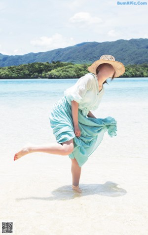A woman in a straw hat sitting on a beach.