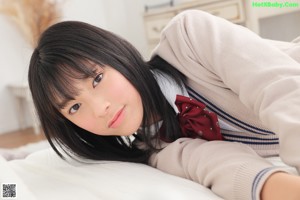 A young woman wearing a beige cardigan and a red bow tie.