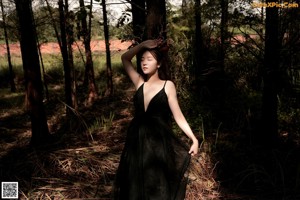 A woman in a black dress standing next to a tree.