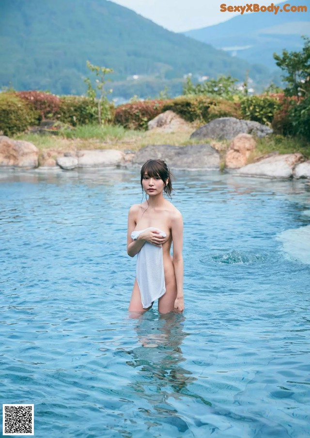 A woman standing in a body of water holding a towel.