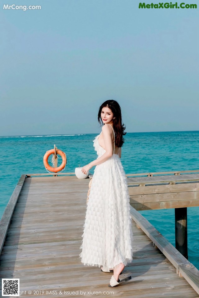 A woman in a white dress standing on a wooden pier.