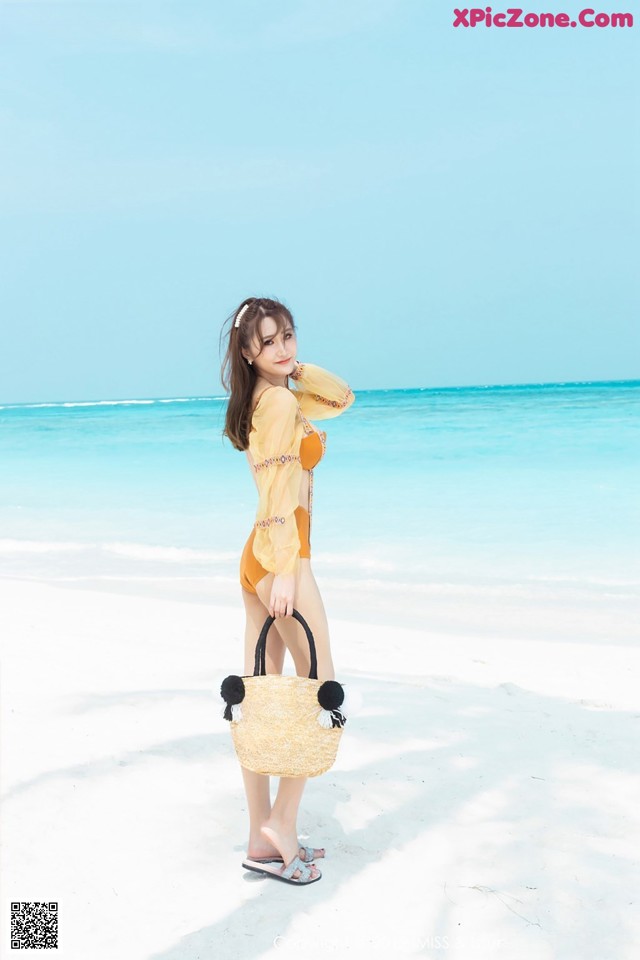 A woman standing on a beach holding a bag.