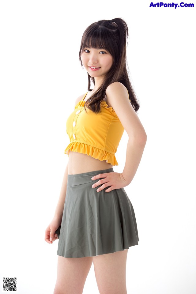 A woman in a yellow top and gray skirt posing for a picture.